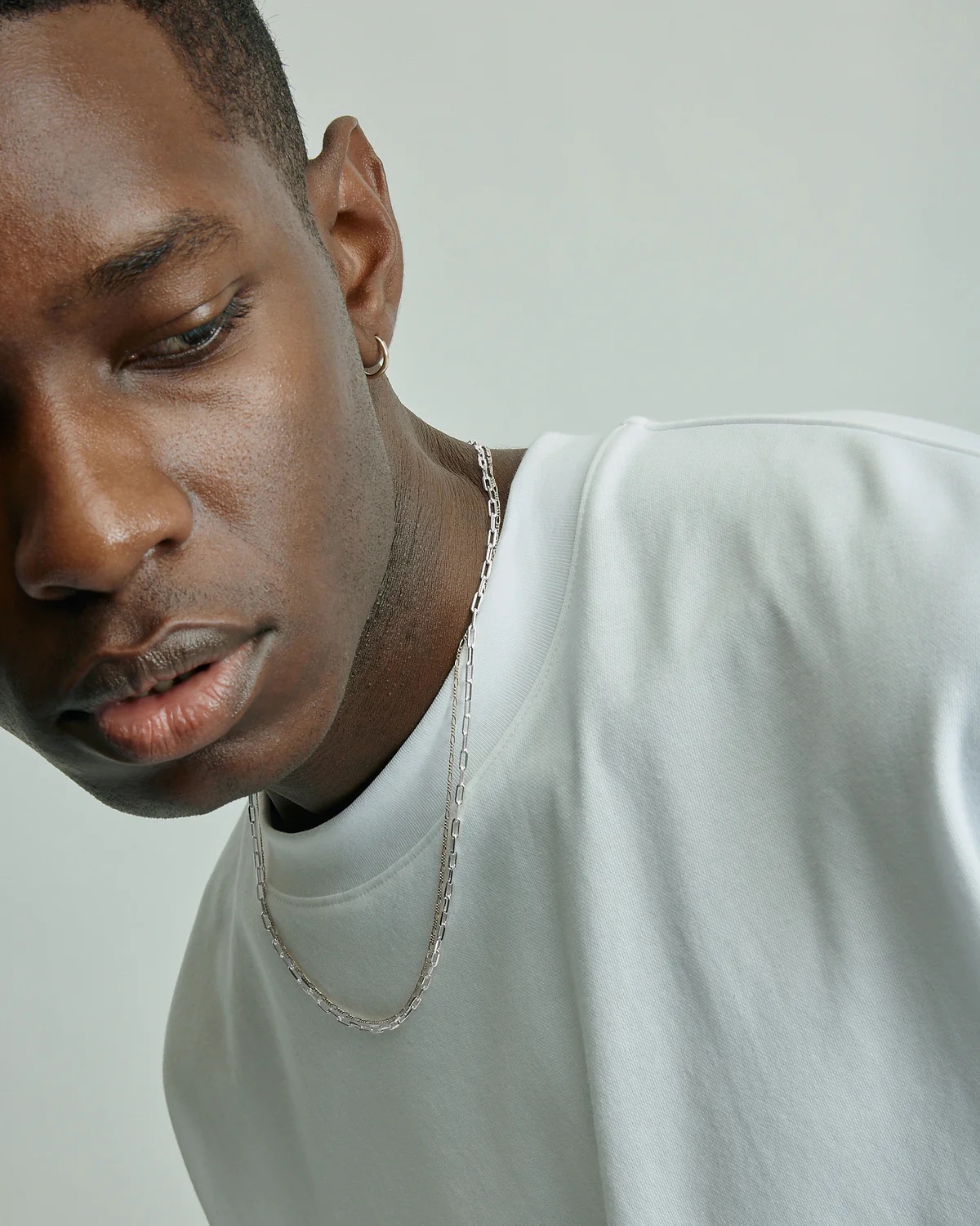 A man wearing silver chains looks away.