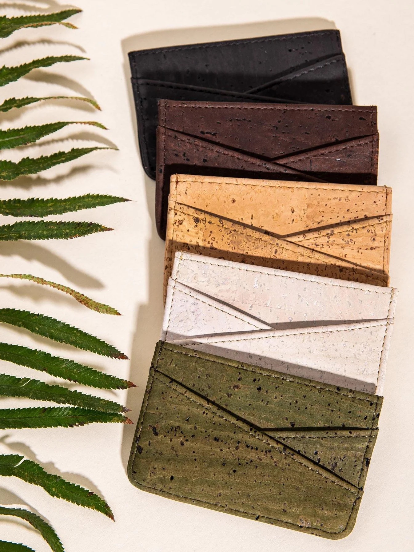 A line of different colored cork wallets on a table next to a plant.