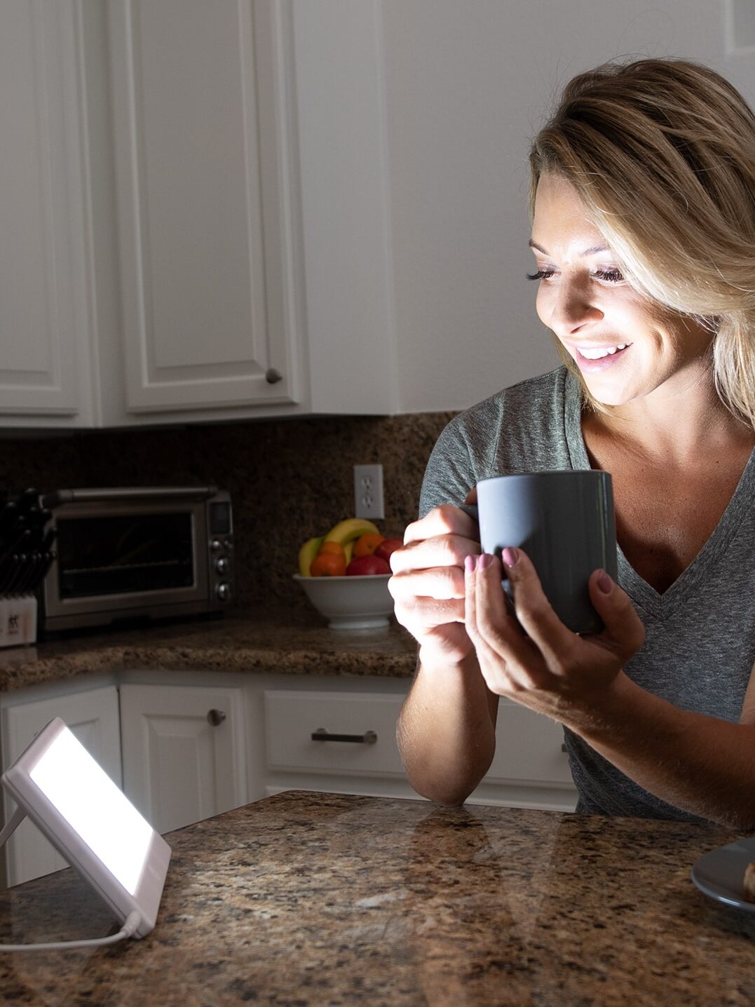 A model smiling, holding a mug, and looking at an Alaska Northern Lights lamp.