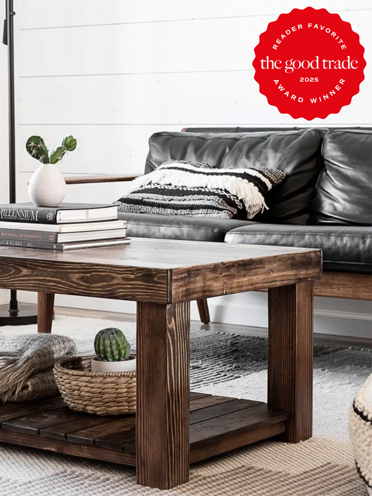 Cozy living room with a black leather sofa, wooden coffee table, books, a vase, and a blanket. "The Good Trade Reader Favorite Award Winner 2025" seal in the corner.
