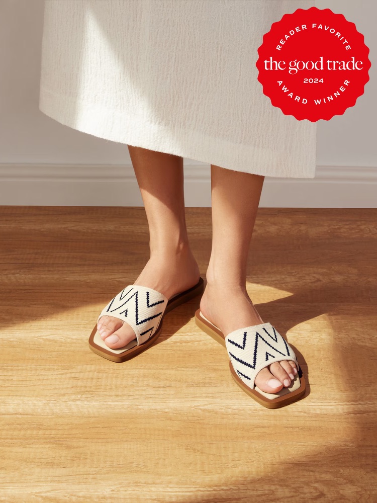 A person wearing a white dress and beige sandals with black zigzag patterns stands on a wooden floor. A red badge in the top-right corner reads, "The Good Trade Reader Favorite Award Winner 2024.