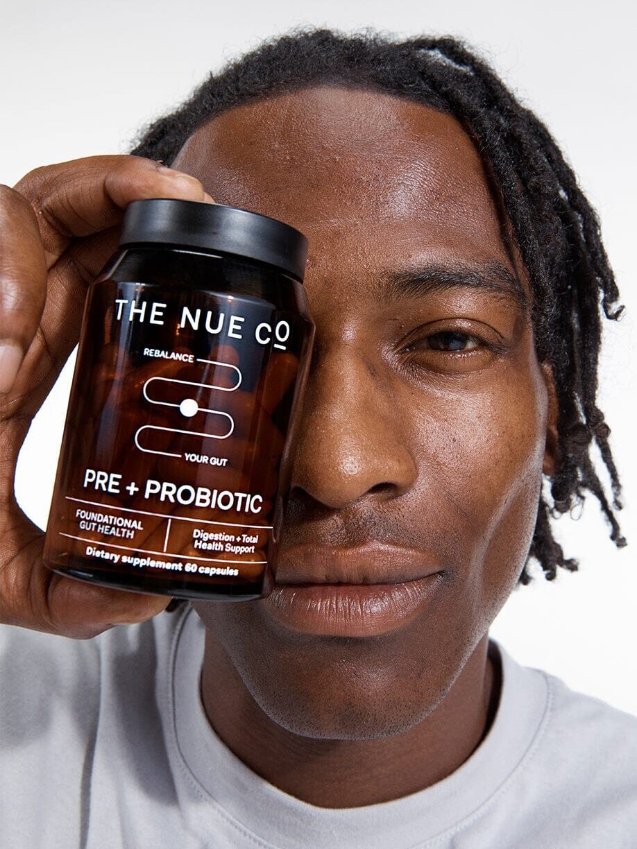 A model holding up a bottle of The Nue Co. probiotics in front of their eye.