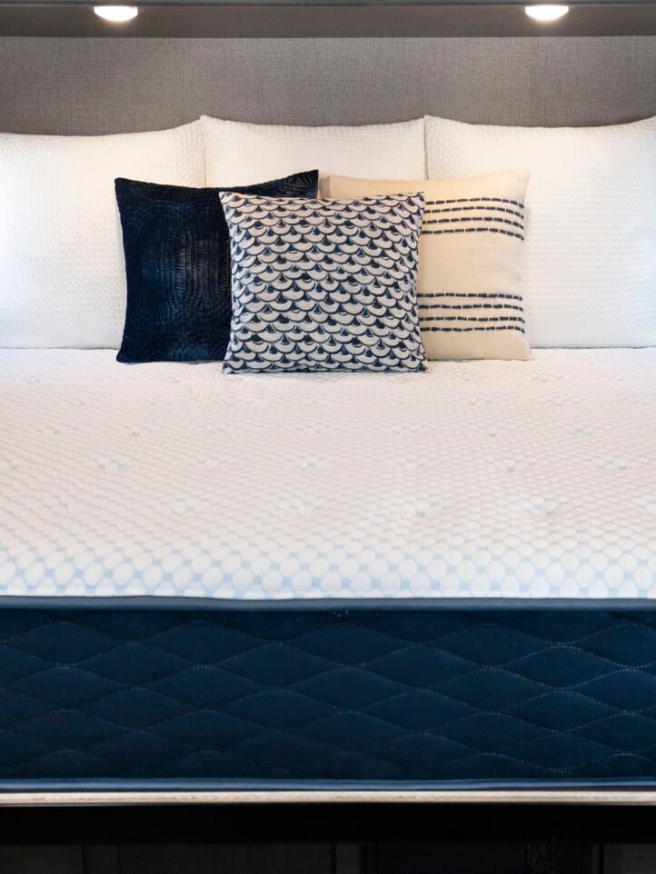 Modern rv bedroom featuring a neatly made bed with a variety of pillows, flanked by small windows and decorative plants.
