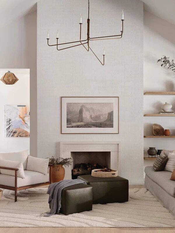 A cozy living room featuring a white fireplace, a vaulted ceiling, modern furniture, and decorative shelving with plants and art pieces.