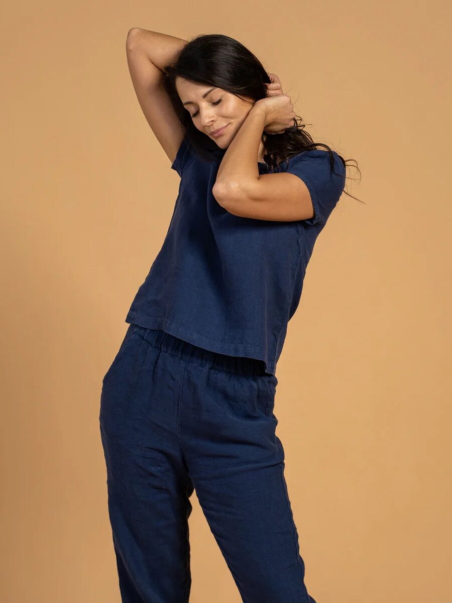 Woman in blue outfit stretching her arms with eyes closed, against a beige background.