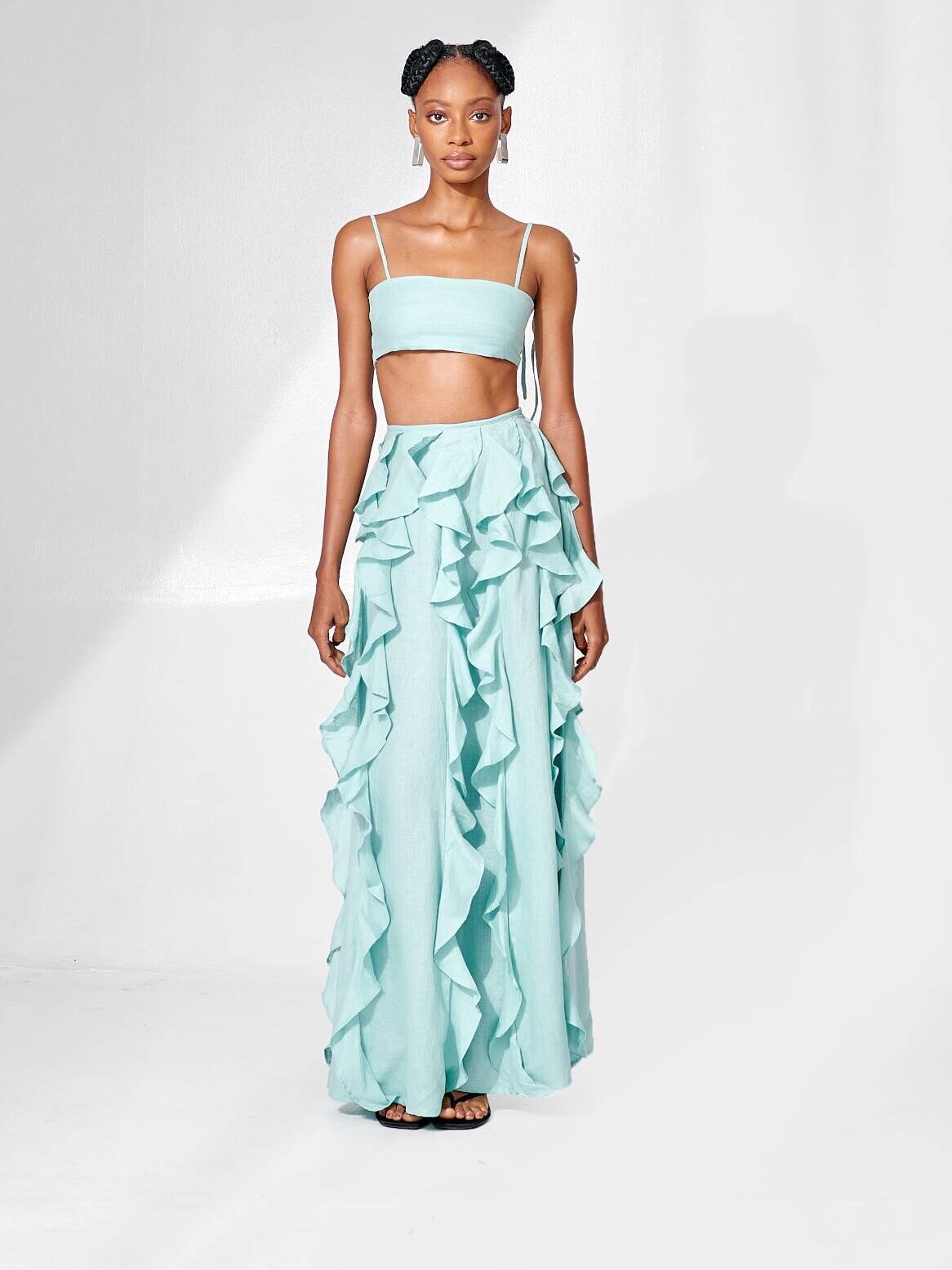 A woman stands confidently in a stylish pale green two-piece outfit with ruffled skirt, on a white background.