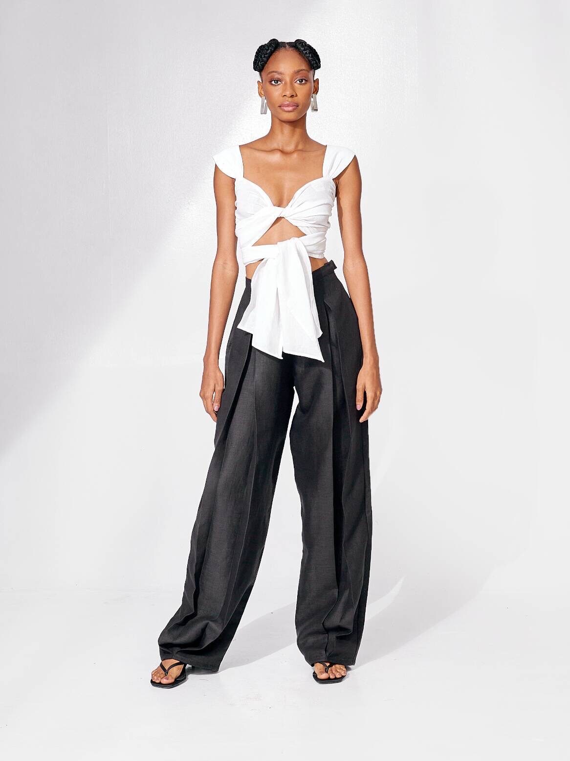 A woman in a unique outfit consisting of a white top with bow details and black wide-leg pants, standing in a white studio setting.