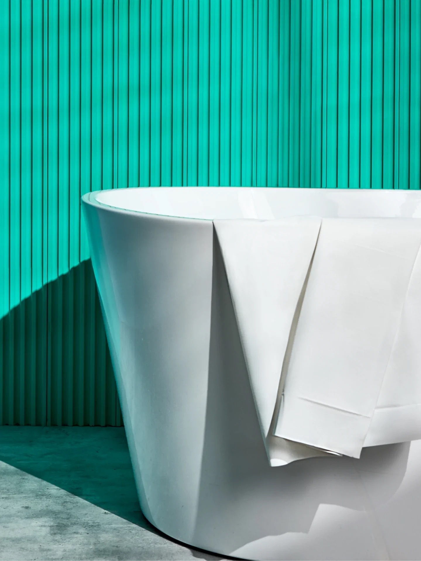 A white bathtub with a white towel draped over the side, set against a turquoise vertical-striped wall.