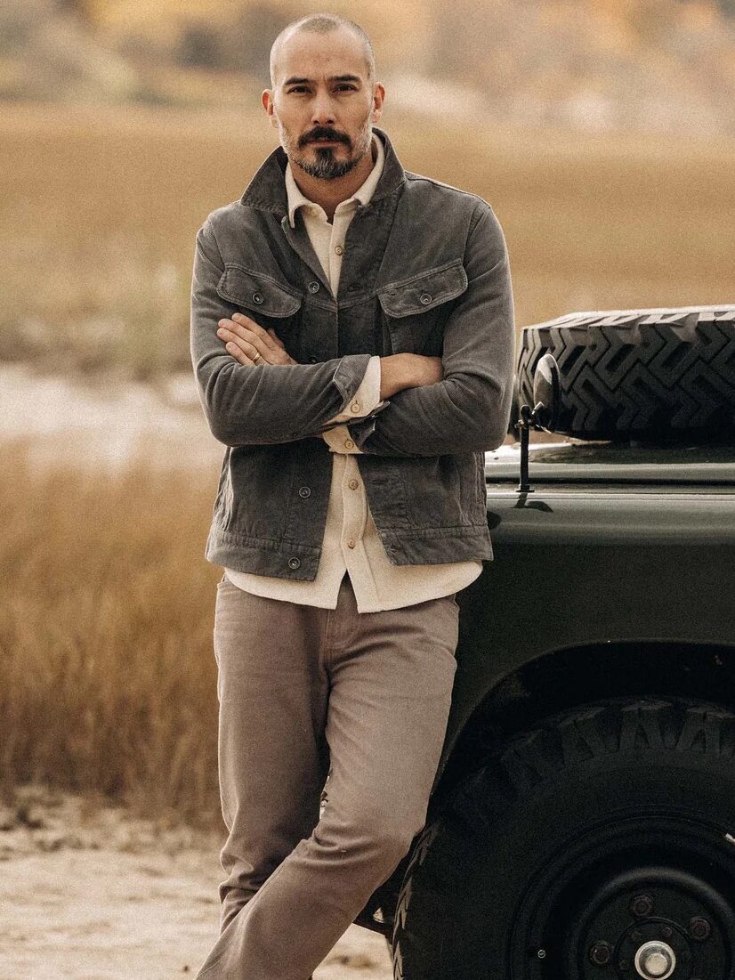 A model leaning against a truck with their arms crossed, wearing a corduroy jacket from Taylor Stitch. 