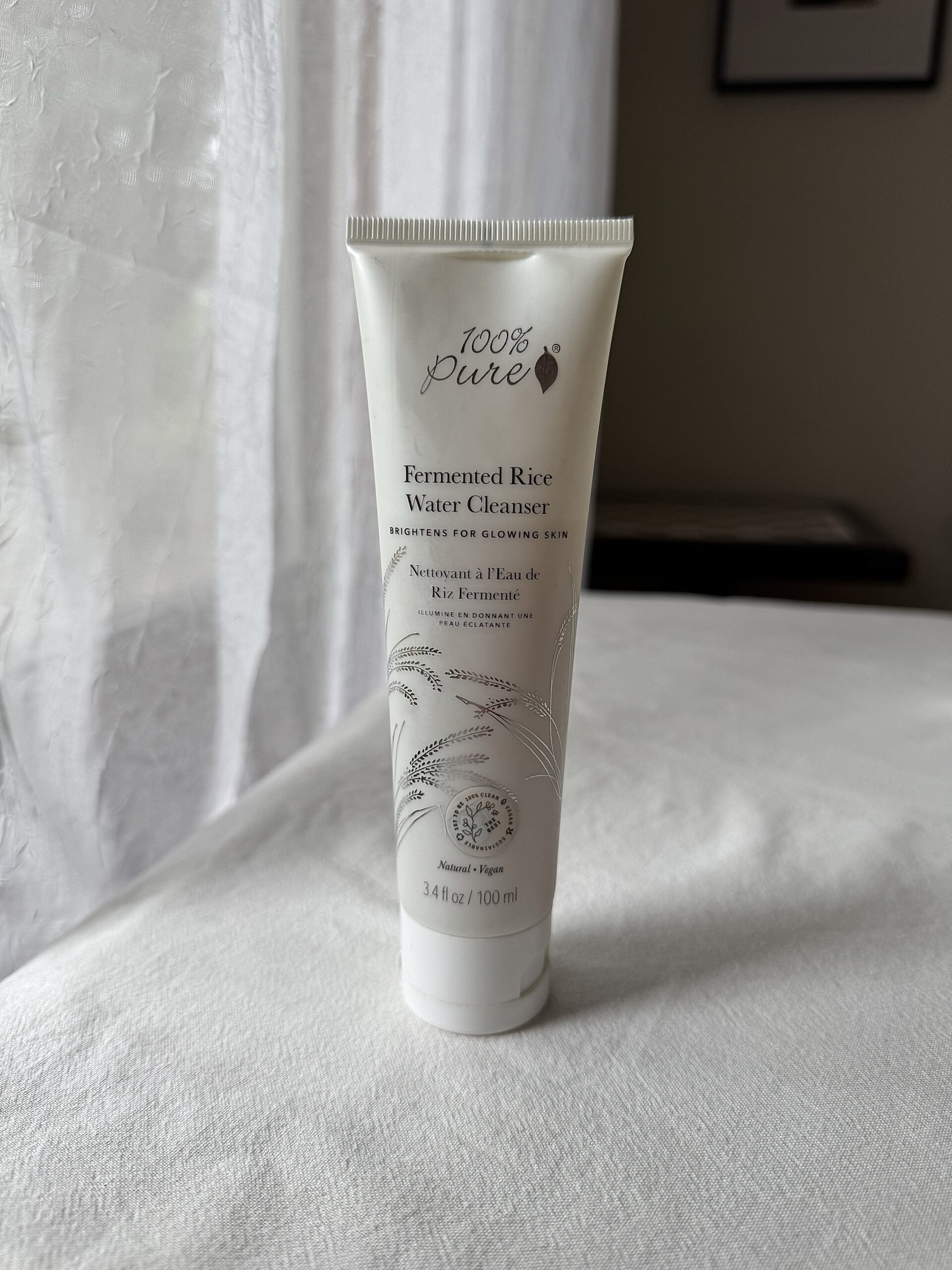 A bottle of 100% Pure face wash on a white fabric surface.