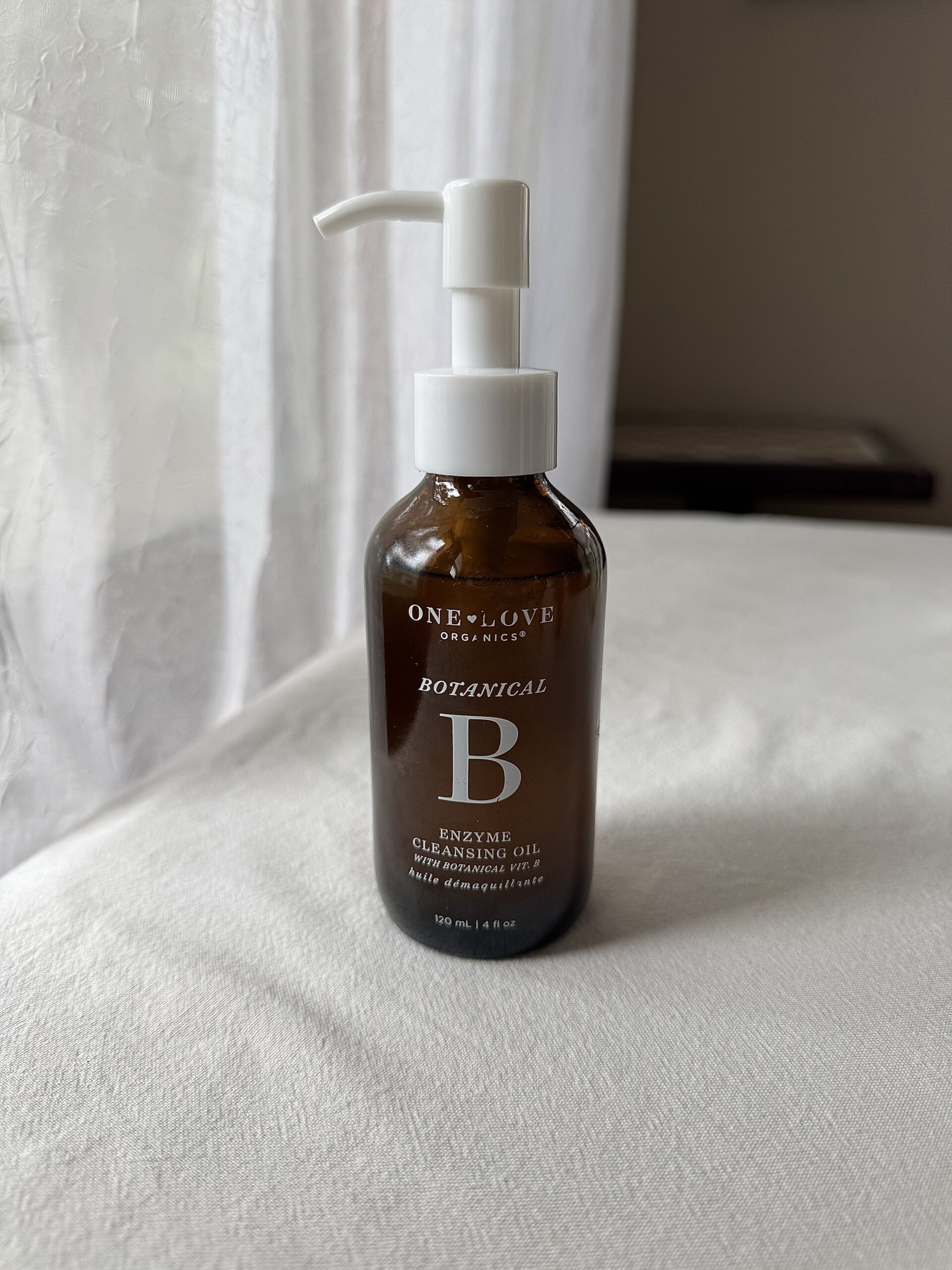 A bottle of One Love Organics face wash sitting on a white fabric surface.