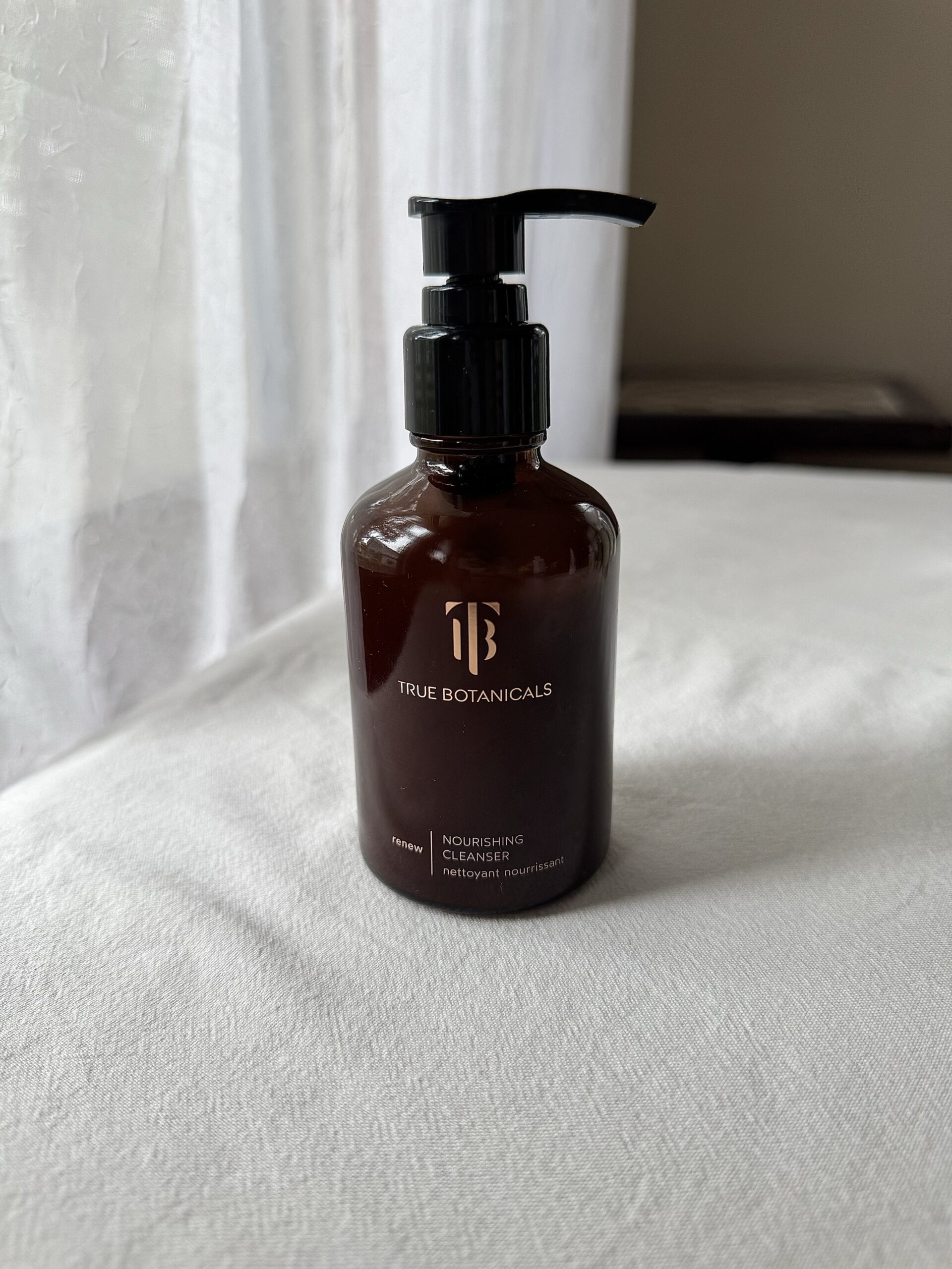 A bottle of True Botanicals face wash on a white fabric surface.