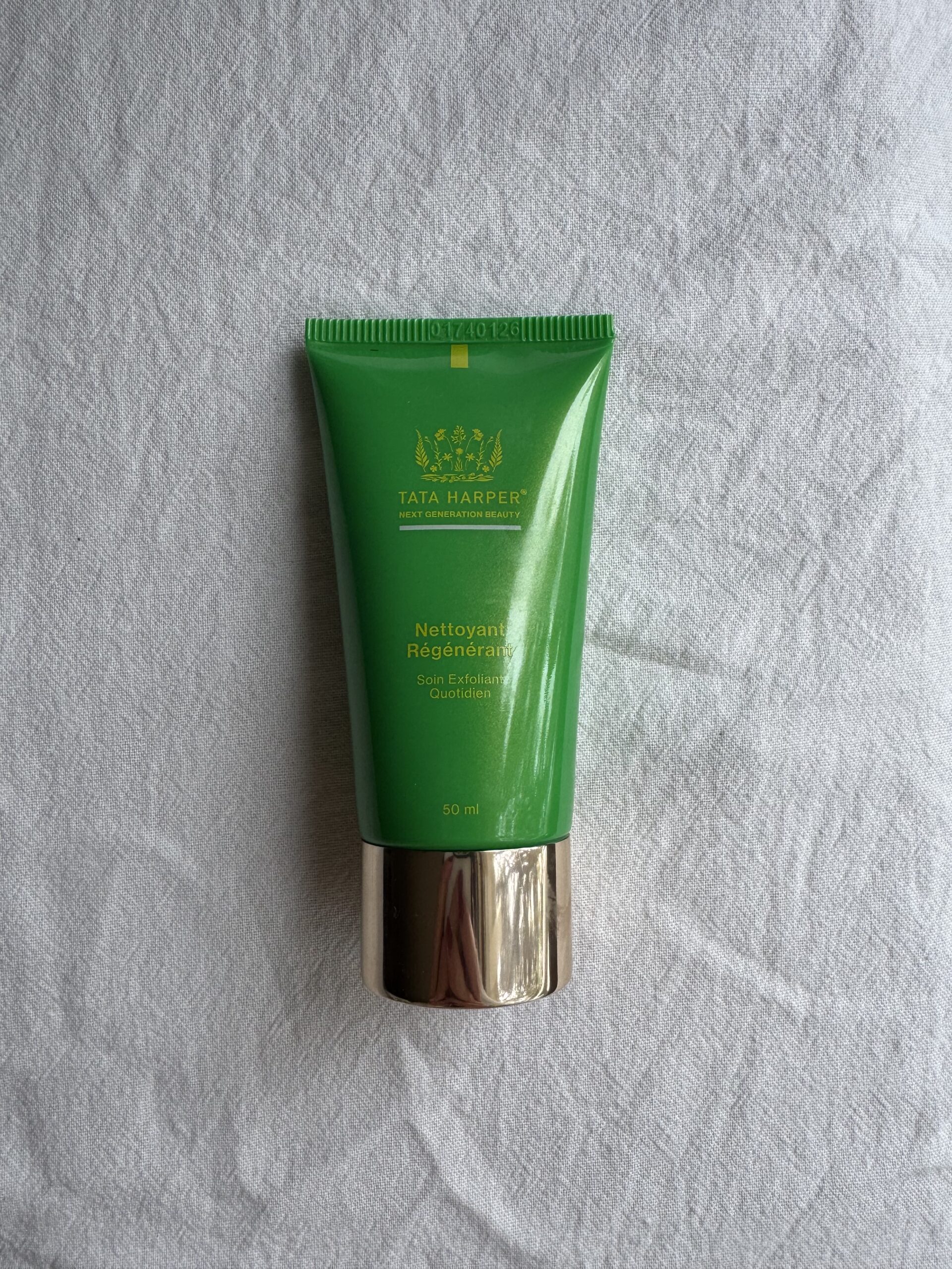A tube of Tata Harper face wash on a white fabric surface.