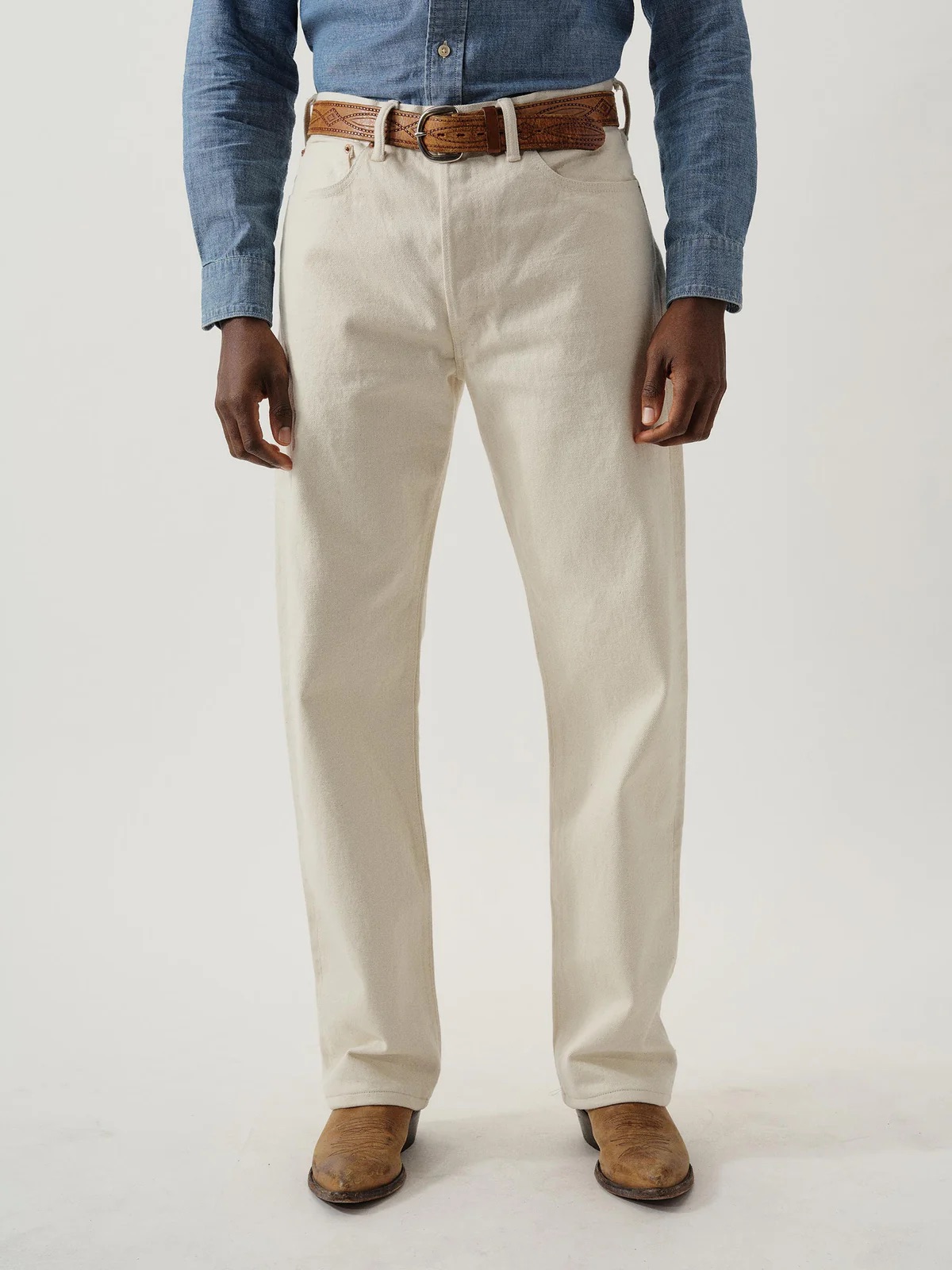 Person wearing a light blue long-sleeve shirt, white pants, a brown belt, and brown shoes, standing against a plain background.