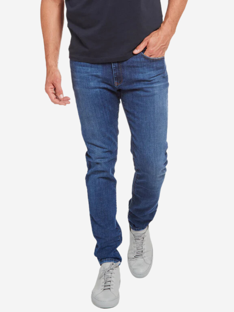A person wearing blue jeans, a black shirt, and white sneakers is walking. The view is from waist down.