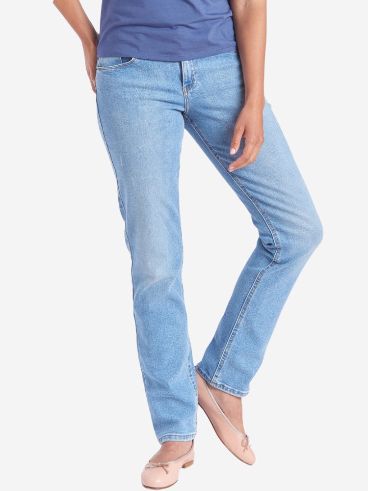 A person wearing light blue jeans, a dark blue shirt, and beige flats stands with one leg slightly crossed in front of the other.