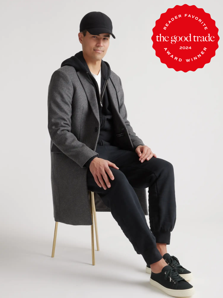 A model, seated, wearing a pair of black Quince sneakers.