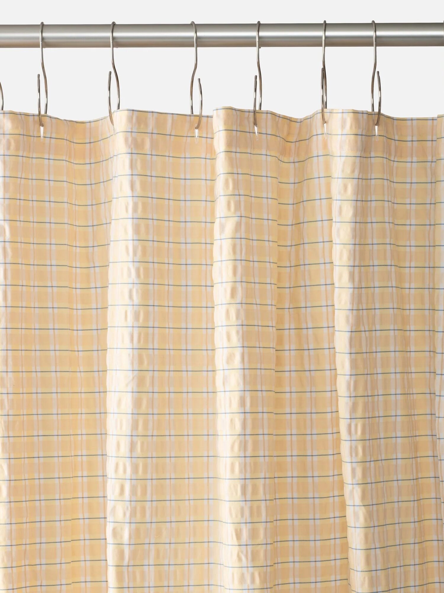 A beige shower curtain with a blue and white checkered pattern, hanging from silver hooks on a metal rod.