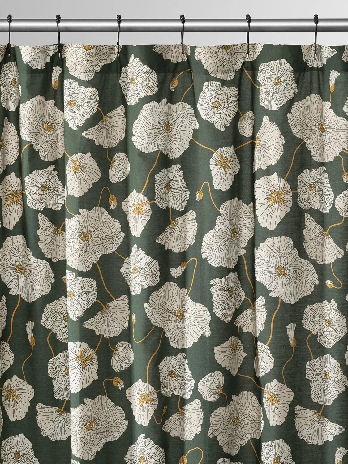 A dark green shower curtain with a white floral pattern hung on a silver rod with black hooks.