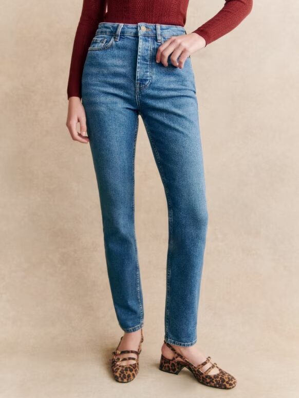 Person wearing a maroon long-sleeve top, high-waisted blue jeans, and leopard print shoes stands against a beige background.