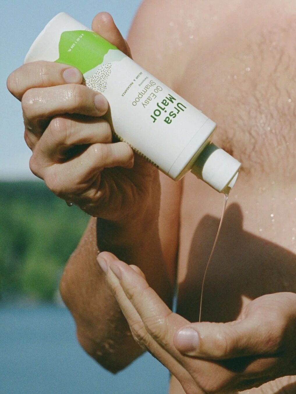 A model squeezing a bottle of Ursa Major shampoo into their hand.