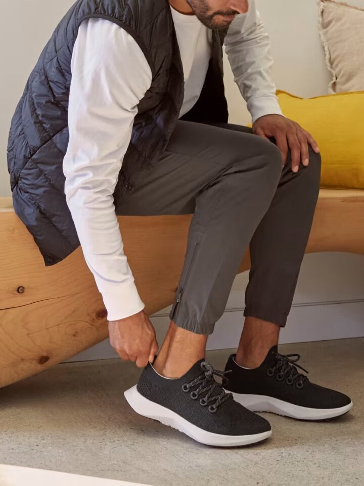 A model putting on a pair of black Allbirds shoes.