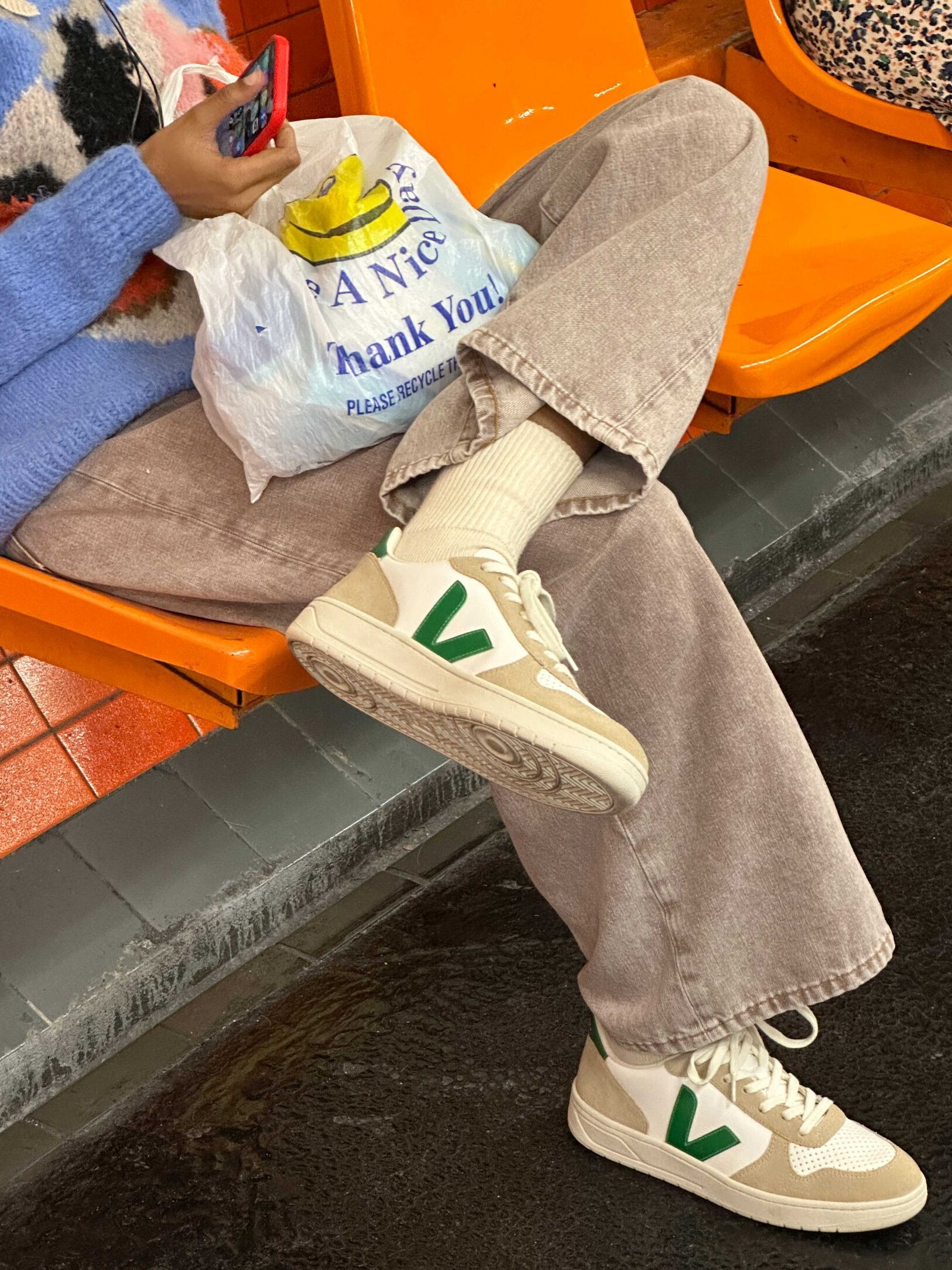 A model sitting on a bench wearing beige, white, and green Veja sneakers.