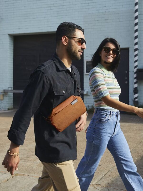 A model wearing a Bellroy sling bag. Another person walks next to them.