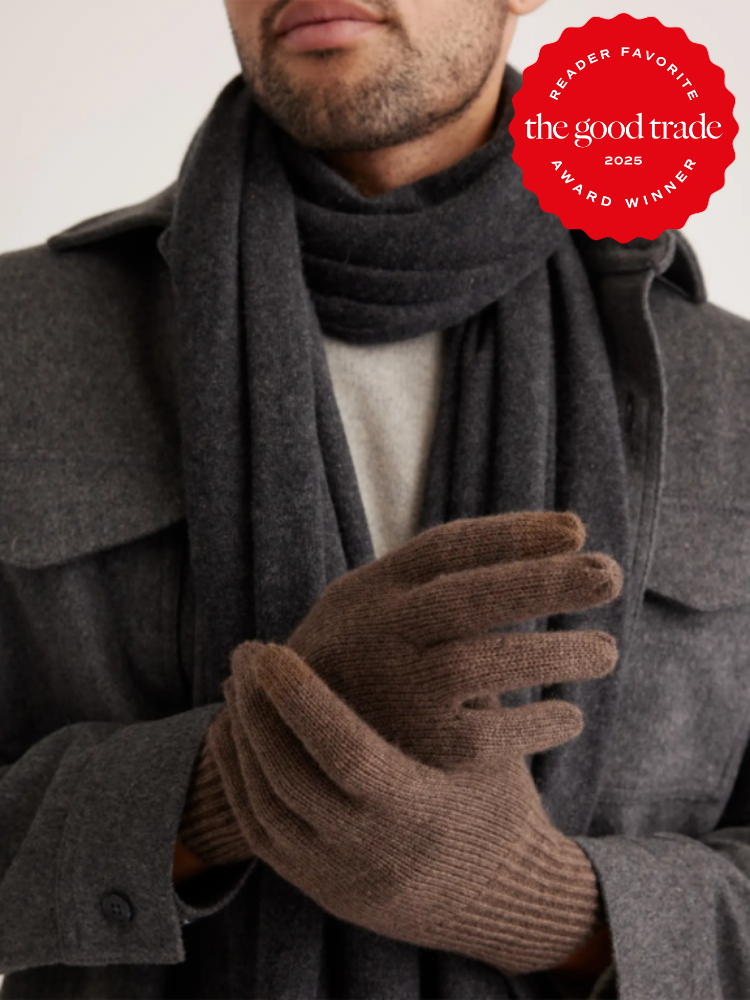 A person in a gray coat and dark scarf, wearing brown gloves, with an award badge for "the good trade" 2025 in the corner.