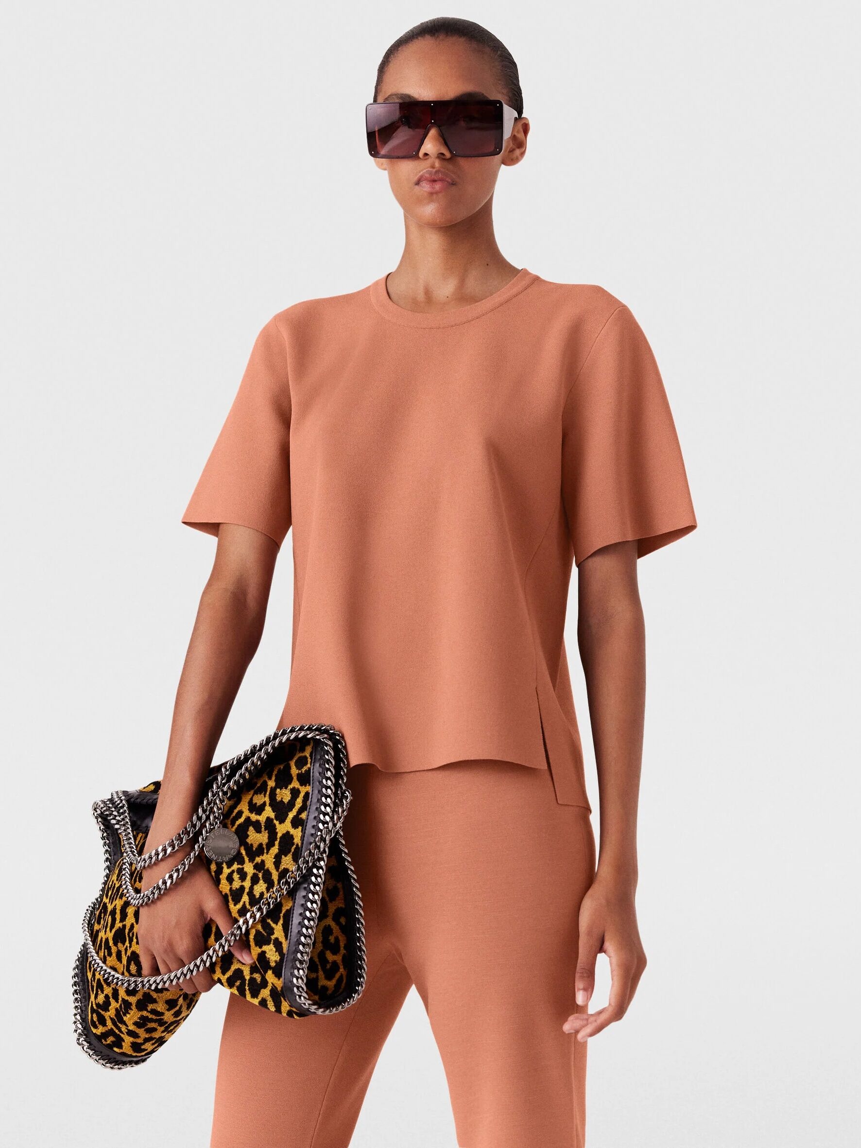 Person wearing a salmon-colored outfit and oversized sunglasses holds a leopard print handbag with chain details.