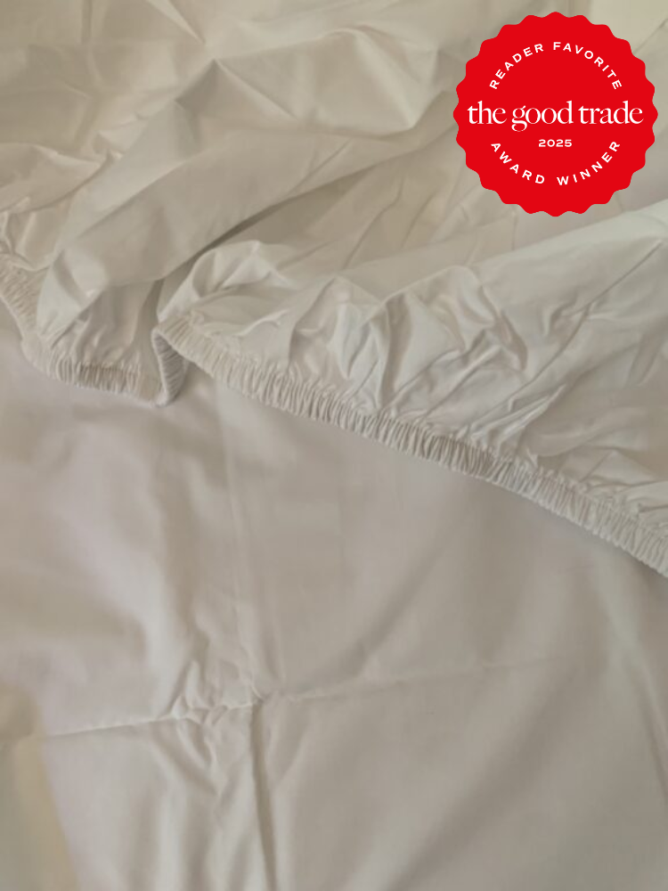 White fitted sheet with elastic corners on a bed. A red badge in the corner reads, "Reader Favorite, The Good Trade, 2025 Award Winner.