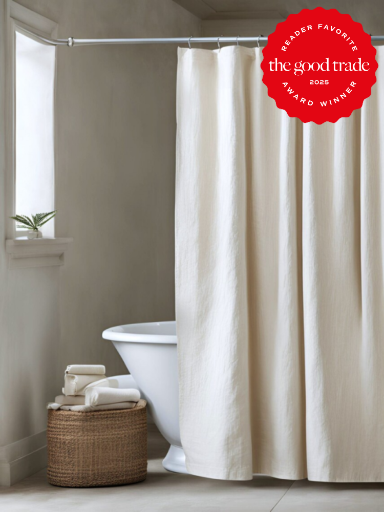 Bathtub with a white curtain partially closed, a wicker basket with towels beside it, and an award emblem in the top corner.