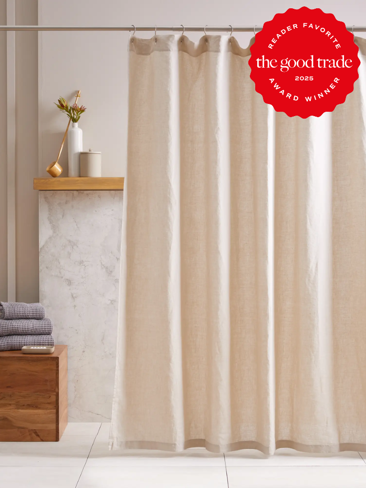 Beige curtain hanging from a rod in a minimalist bathroom with folded towels and a vase on a wooden shelf. Red award badge in the corner.