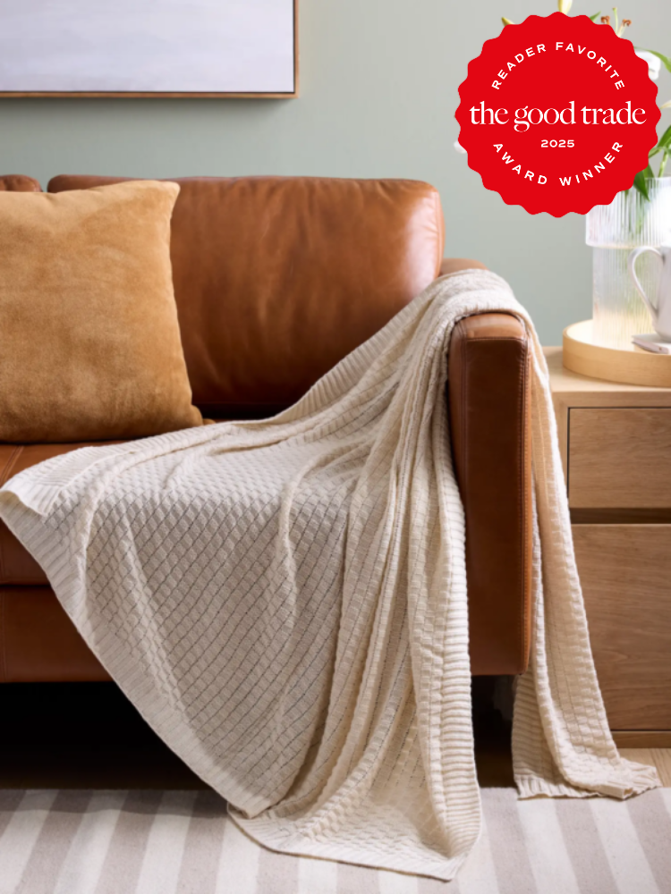 A brown leather couch with beige pillows and a cream waffle-textured throw blanket. A wooden side table is to the right. A red award badge is in the top right corner.