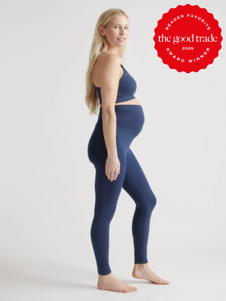 Pregnant woman in blue activewear poses sideways against a plain background. A red award emblem is visible in the top right corner.