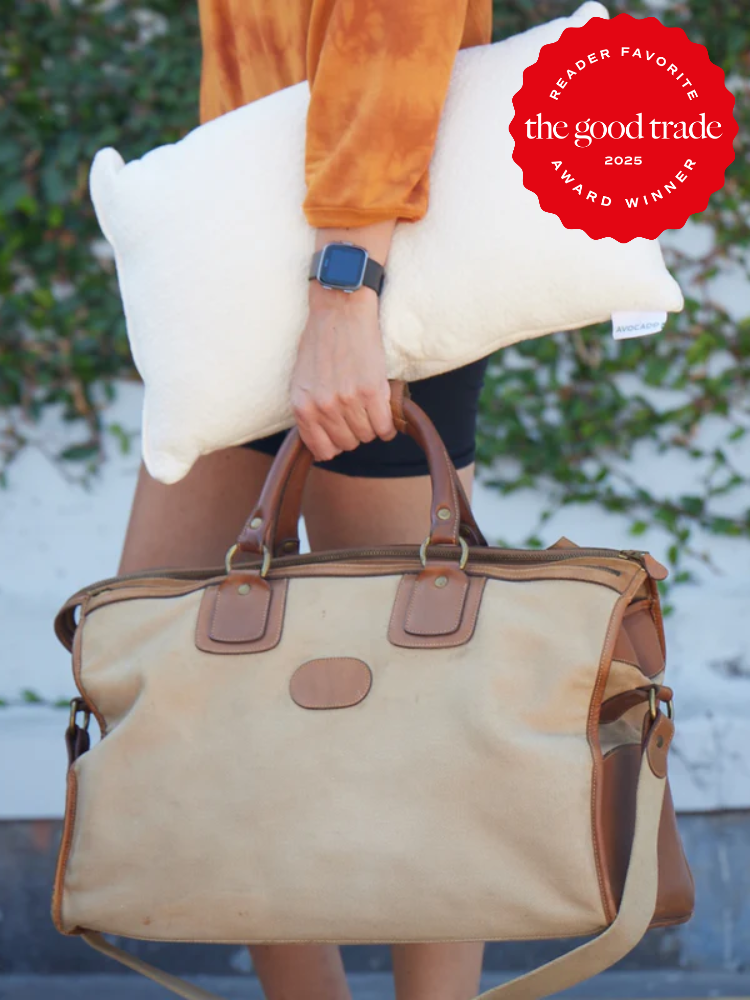 Person holding a beige and brown leather travel bag and a white pillow, with a reader favorite award badge from The Good Trade on the top right.