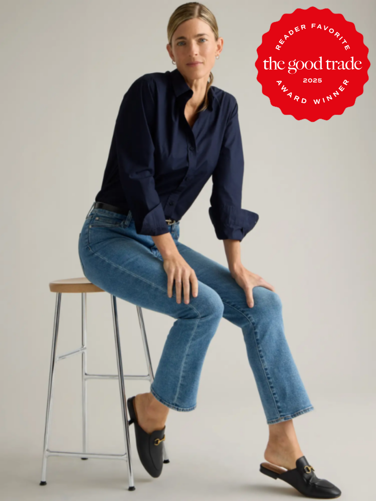 Person sitting on a wooden stool, wearing a navy shirt, blue jeans, and black loafers. A red badge on the top right indicates "The Good Trade 2025 Reader Favorite Award Winner.