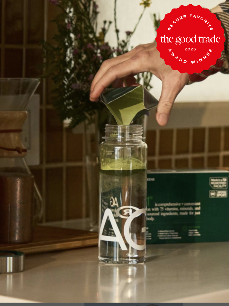 Person pouring a green powder into a clear bottle in a kitchen, with flowers in the background. Red award winner label in the top right corner.