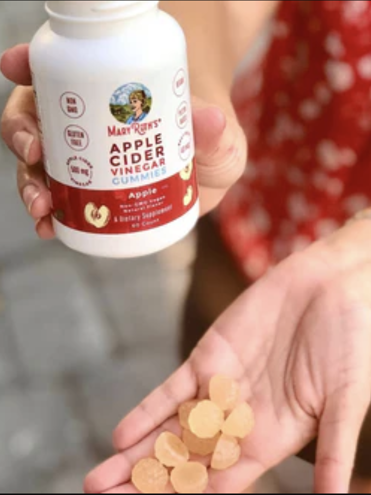 A person holds a bottle of apple cider vinegar gummies and a handful of gummies, outdoors.