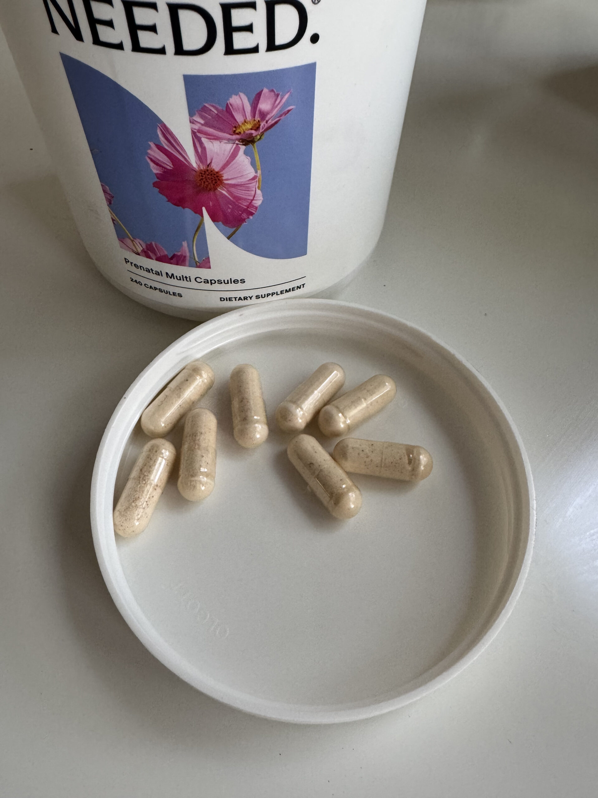 A container labeled "Prenatal Multi Capsules" with eight beige capsules on a white lid.