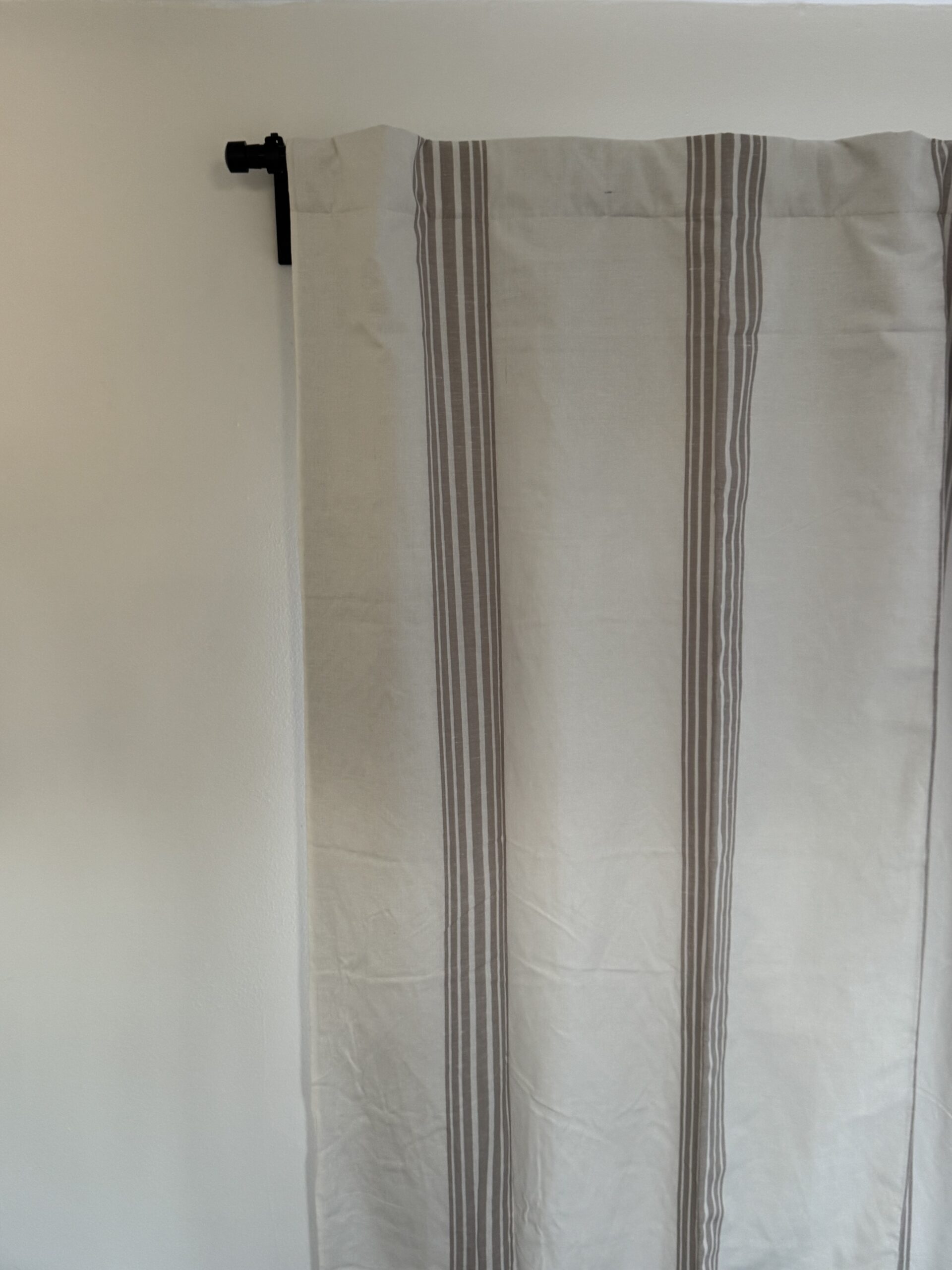 Close-up of a beige curtain with vertical gray stripes hanging on a black rod against a white wall.