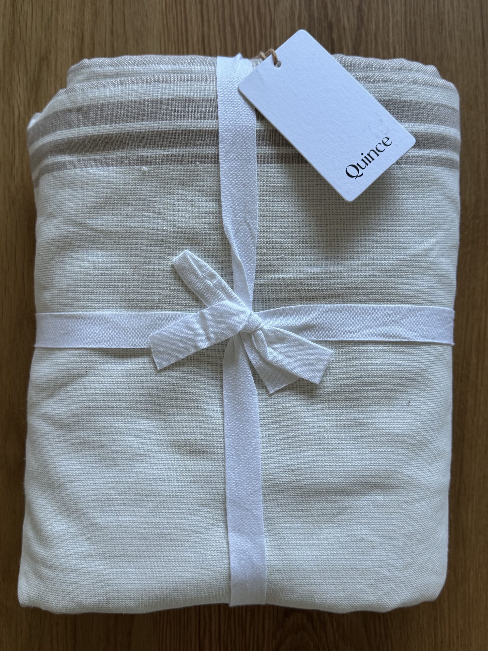 Folded beige linen with striped accents, tied with a white ribbon and tag reading "Quince," placed on a wooden surface.