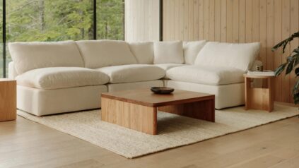 A white sectional sofa and wooden coffee table on a light rug in a room with large windows and wooden walls.