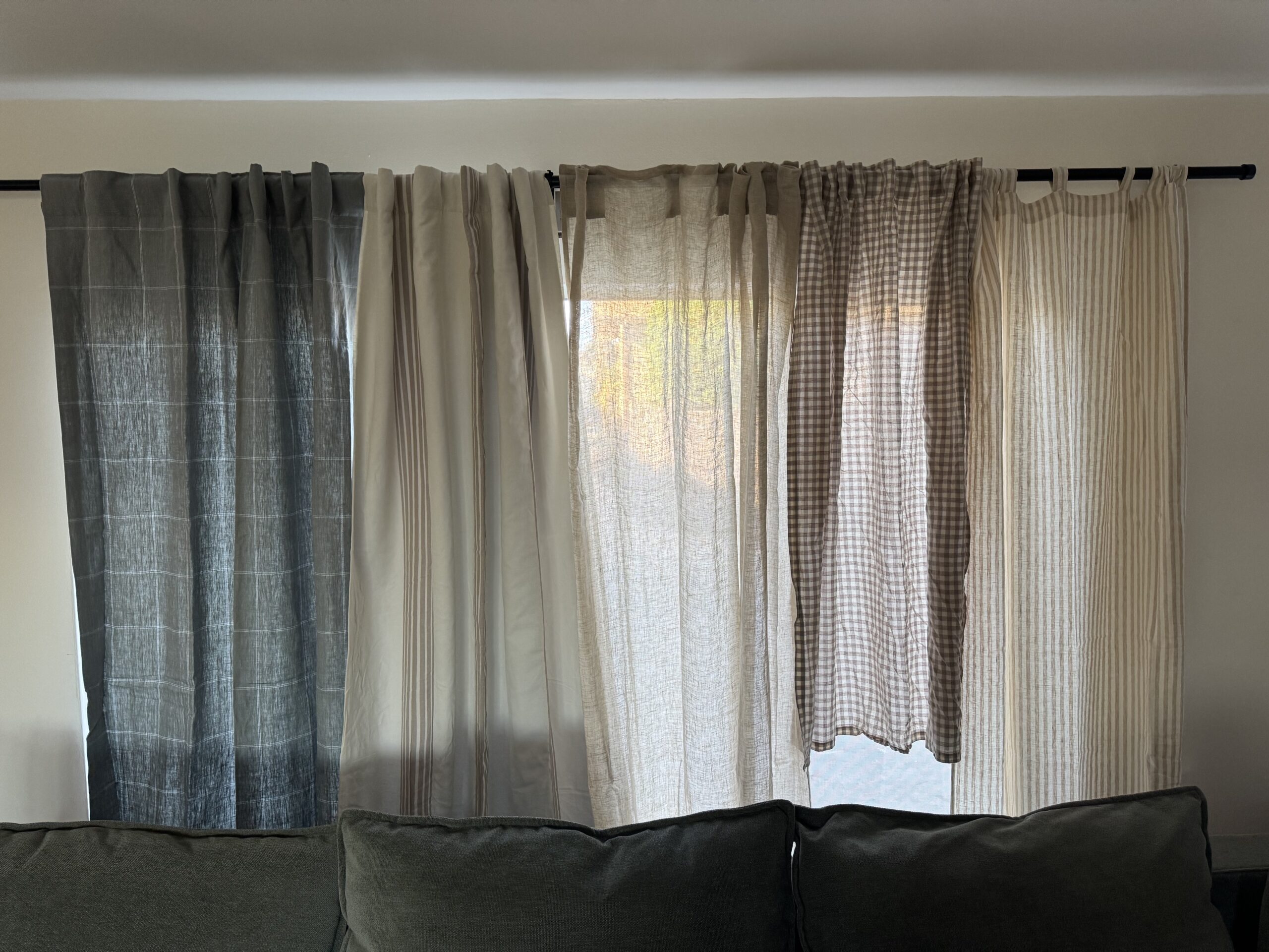 A curtain rod displaying five different curtain panels with varying colors and patterns, hanging above a dark green sofa.