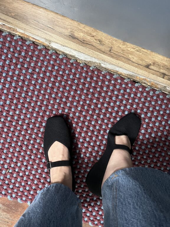 Black shoes on feet standing on a red and gray polka-dotted carpet.