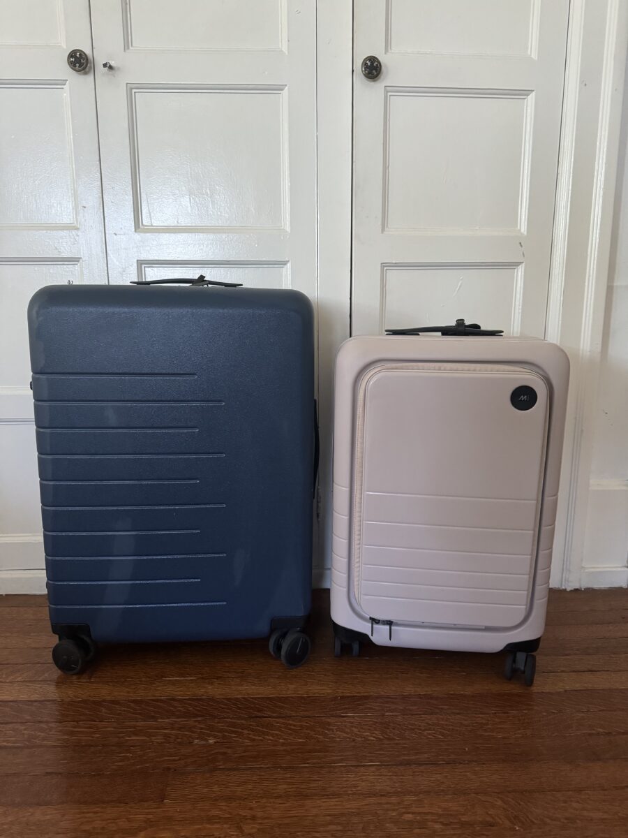 A large navy suitcase and a smaller beige suitcase with wheels stand side by side on a wooden floor in front of white paneled doors.