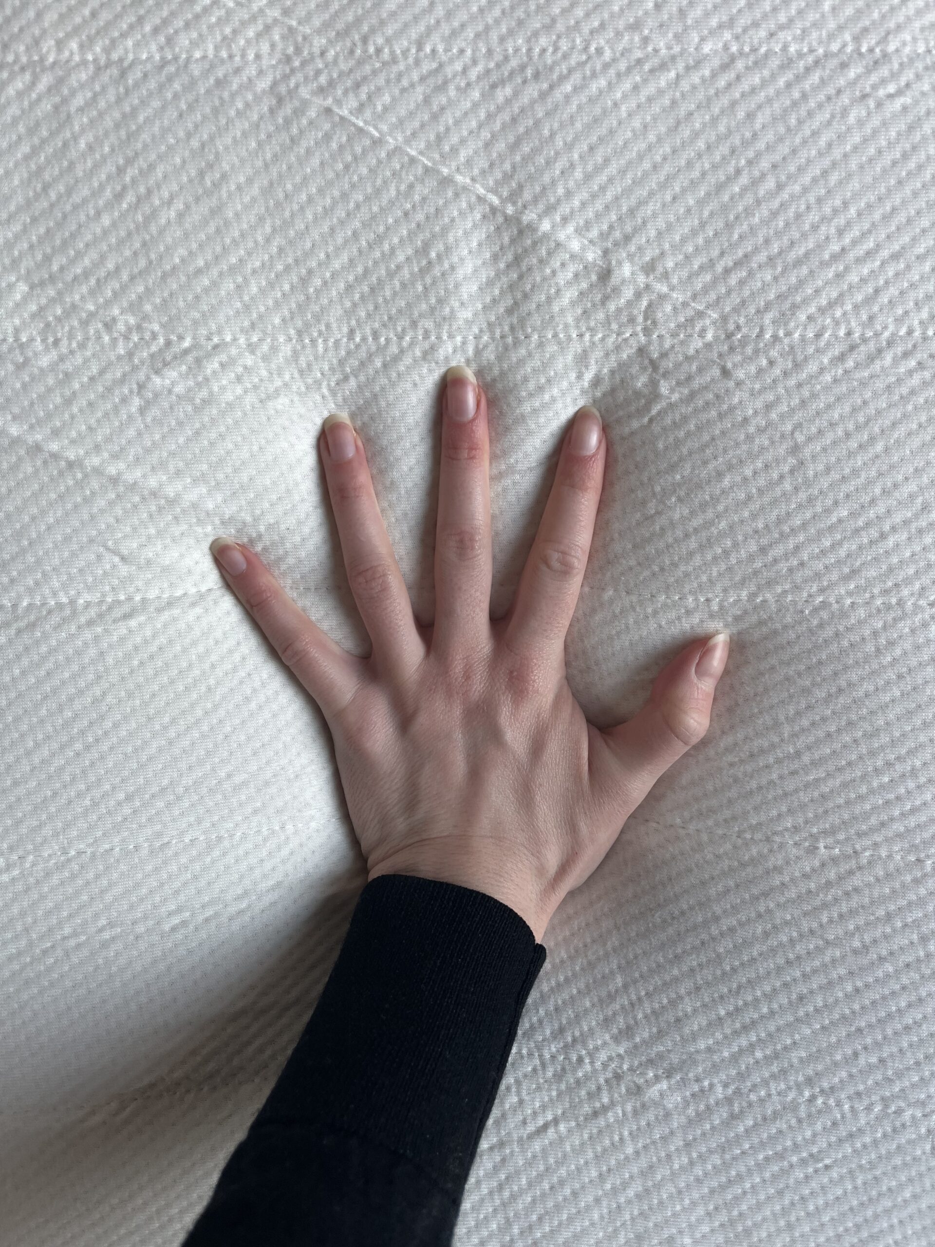 A hand wearing a black sleeve presses down on a white textured surface, creating slight indentations.
