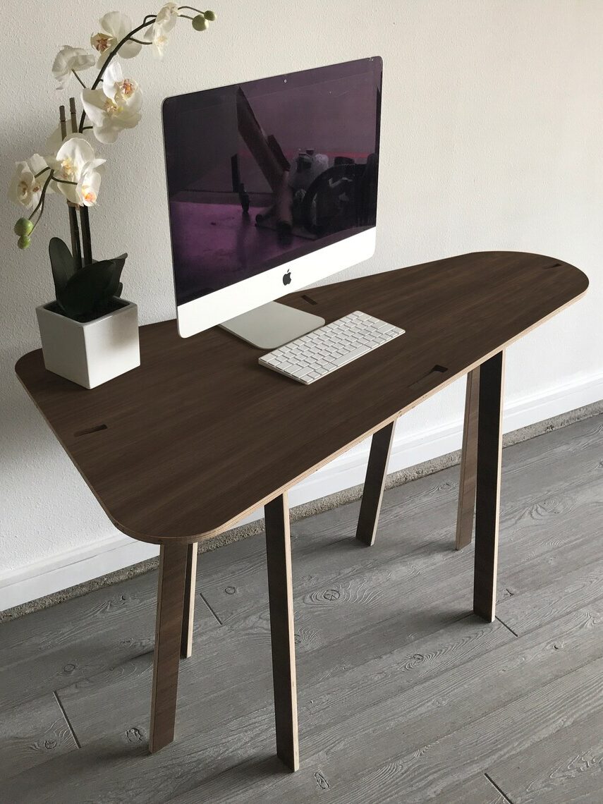 A wooden desk with an iMac, keyboard, and a potted orchid against a white wall on a gray wooden floor.
