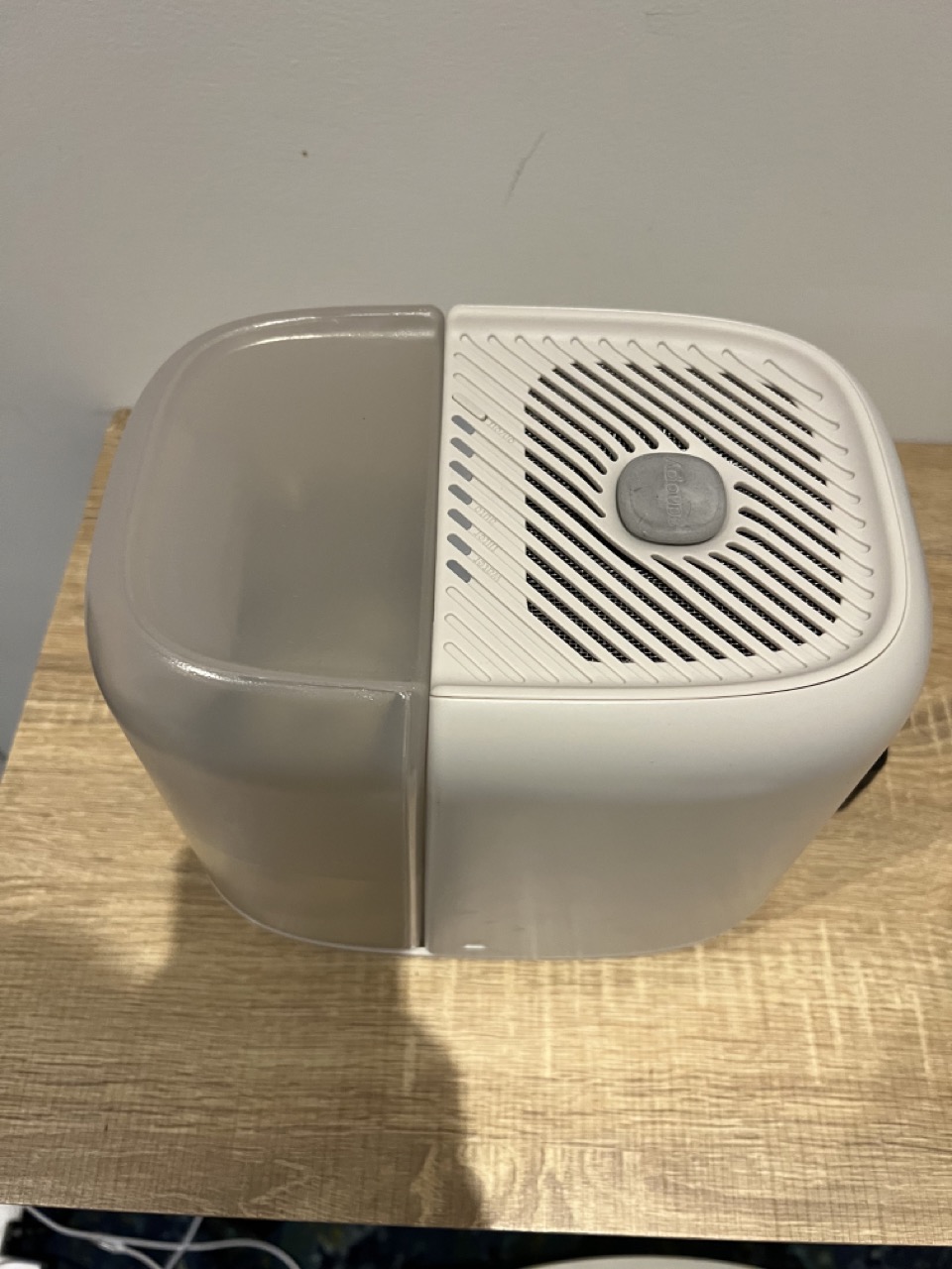 A white dehumidifier with a translucent water tank sits on a light wooden surface against a plain wall.