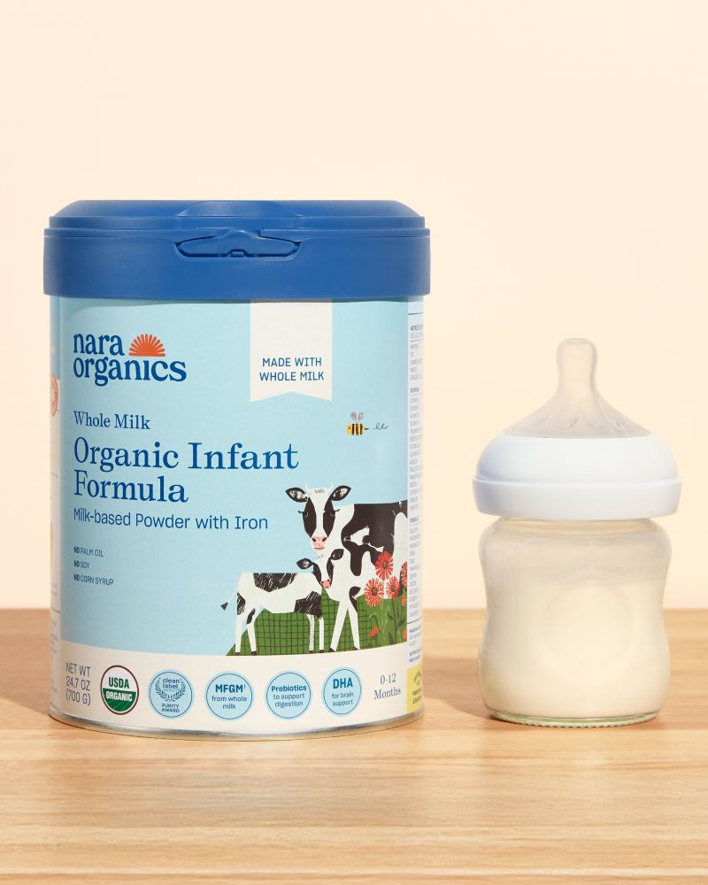 A container of Nara Organics Organic Infant Formula is placed next to a baby bottle filled with formula on a wooden surface.